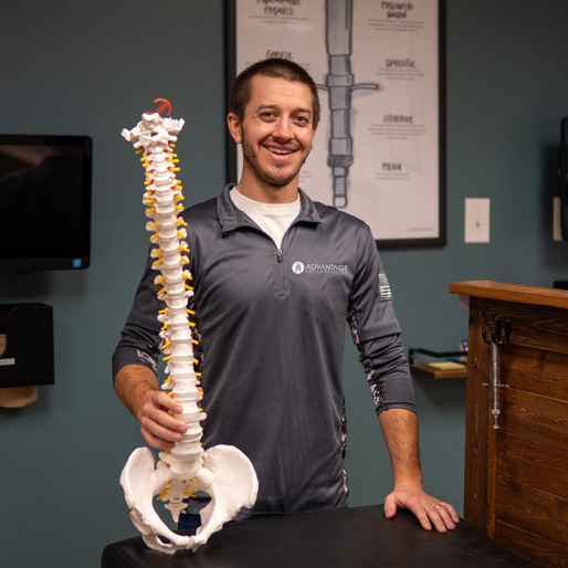 Chiropractor Dr. Zach Bruley of Advantage Health Center in Eau Claire, WI holding a model of a skeletal spine.